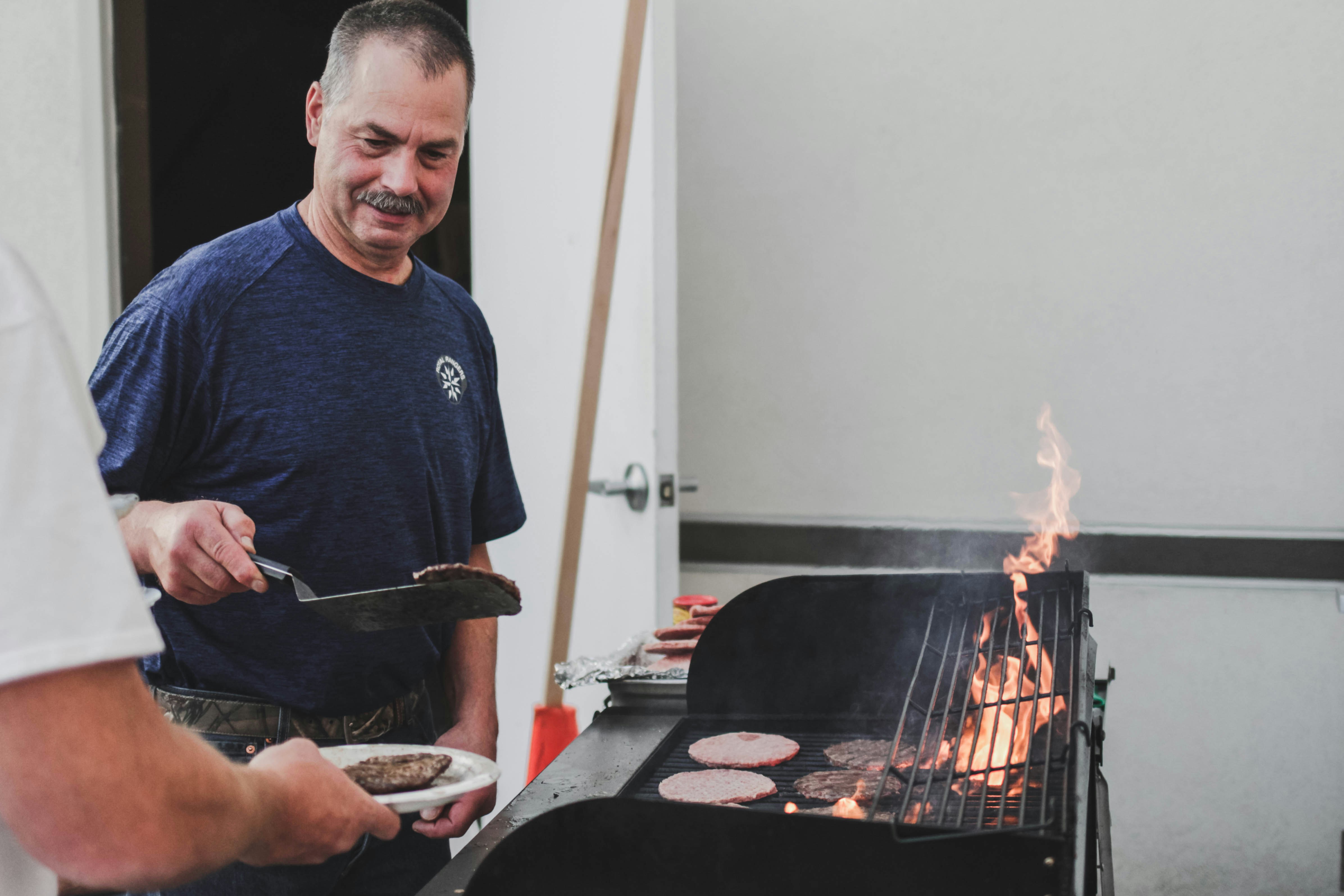 Man moving burgers from a bbq onto a plate
