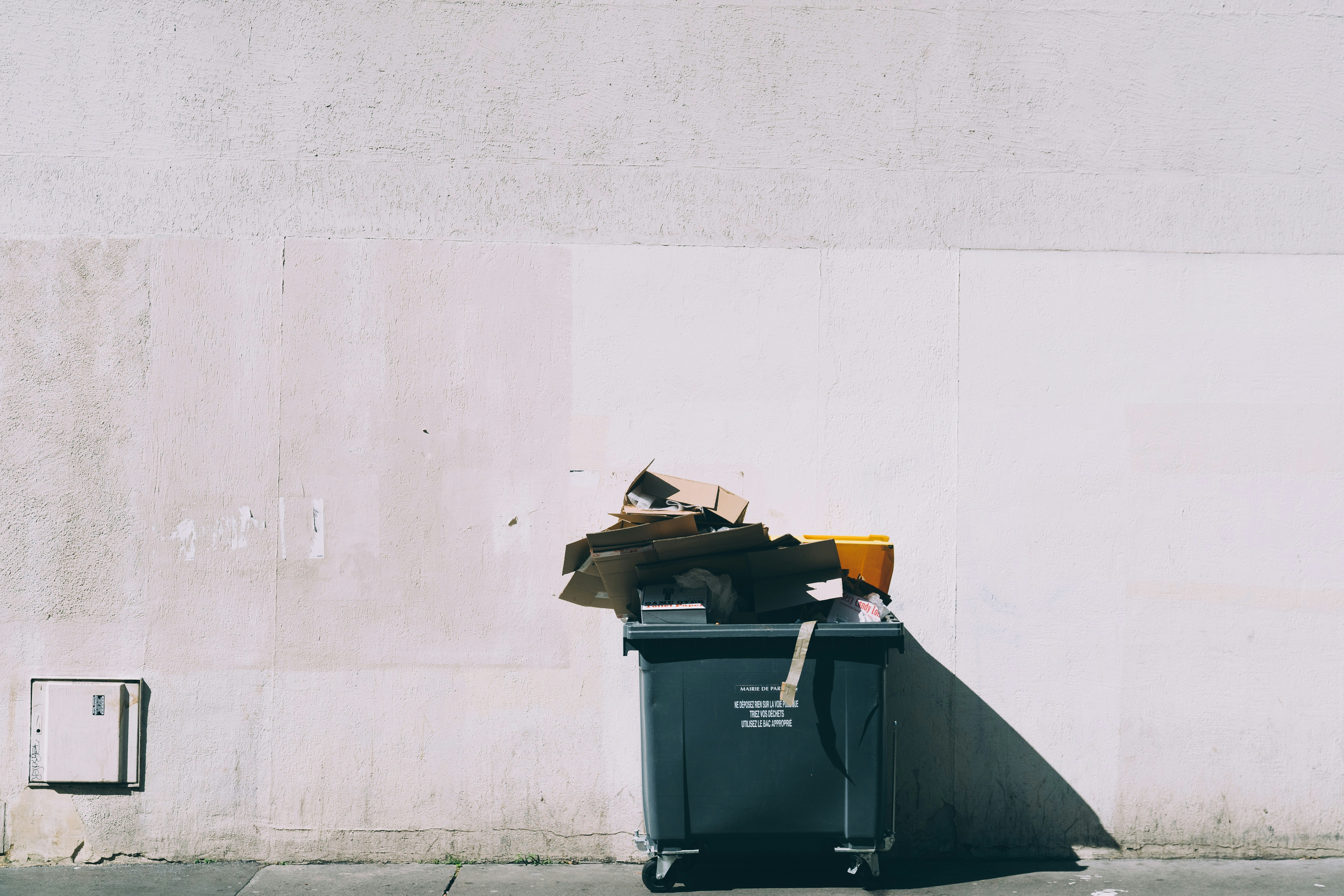 Large waste bin overflowing with rubbish against a plain concrete wall