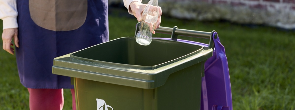 Someone putting a glass bottle in the purple bin