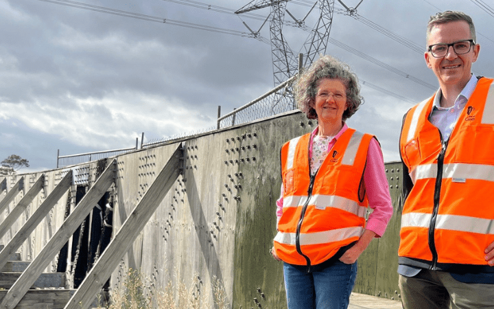 Councillors Ross and Koomen smile in front of the old wooden bridge