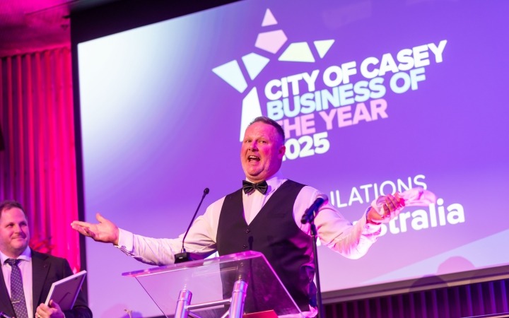 Man in a suit speaking at a podium with his arms outstretched