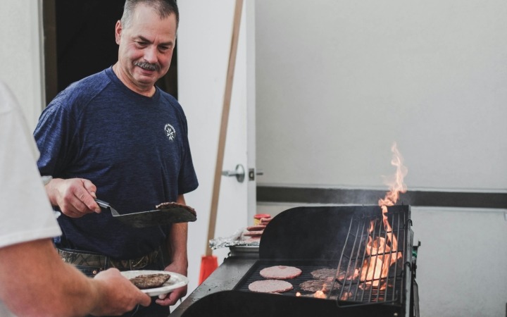 Man moving burgers from a bbq onto a plate