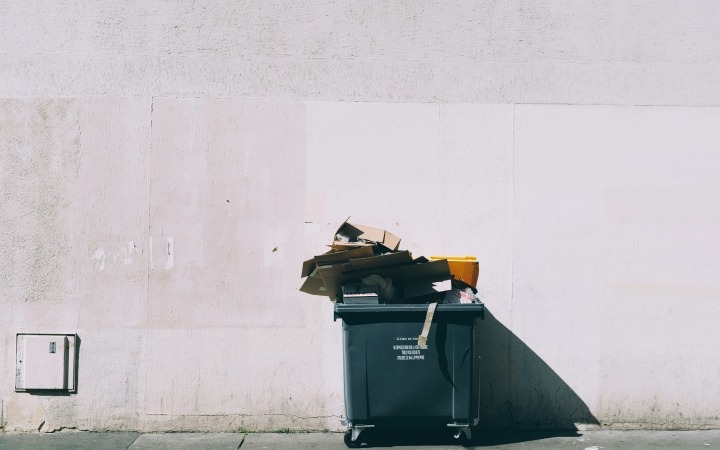 Large waste bin overflowing with rubbish against a plain concrete wall