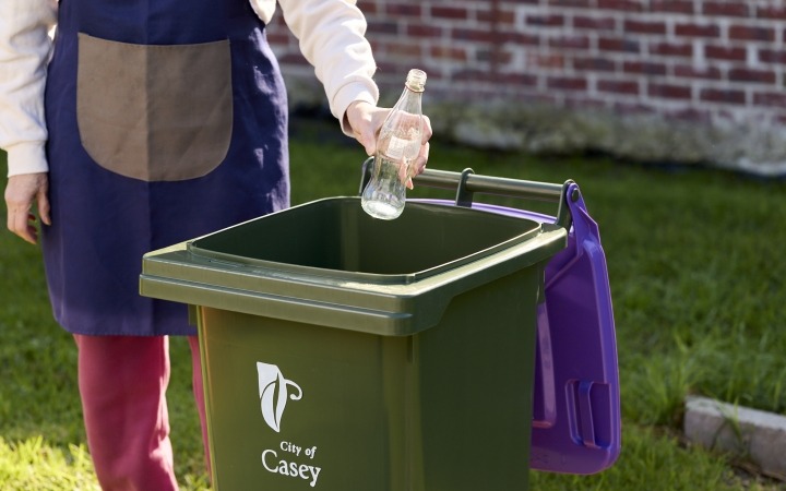 Someone putting a glass bottle in the purple bin